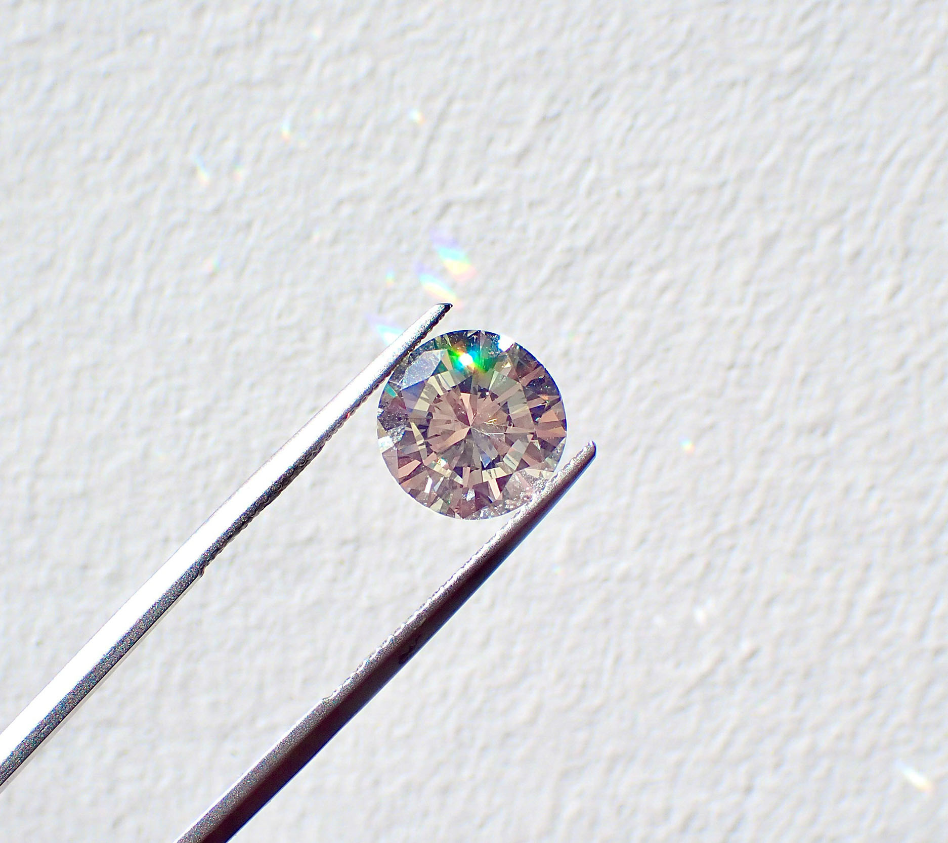 close up of tongs holding up diamond against a white wall, rainbow light reflecting on the white wall, Sheaff Brock investment advisors blog, retail consumers