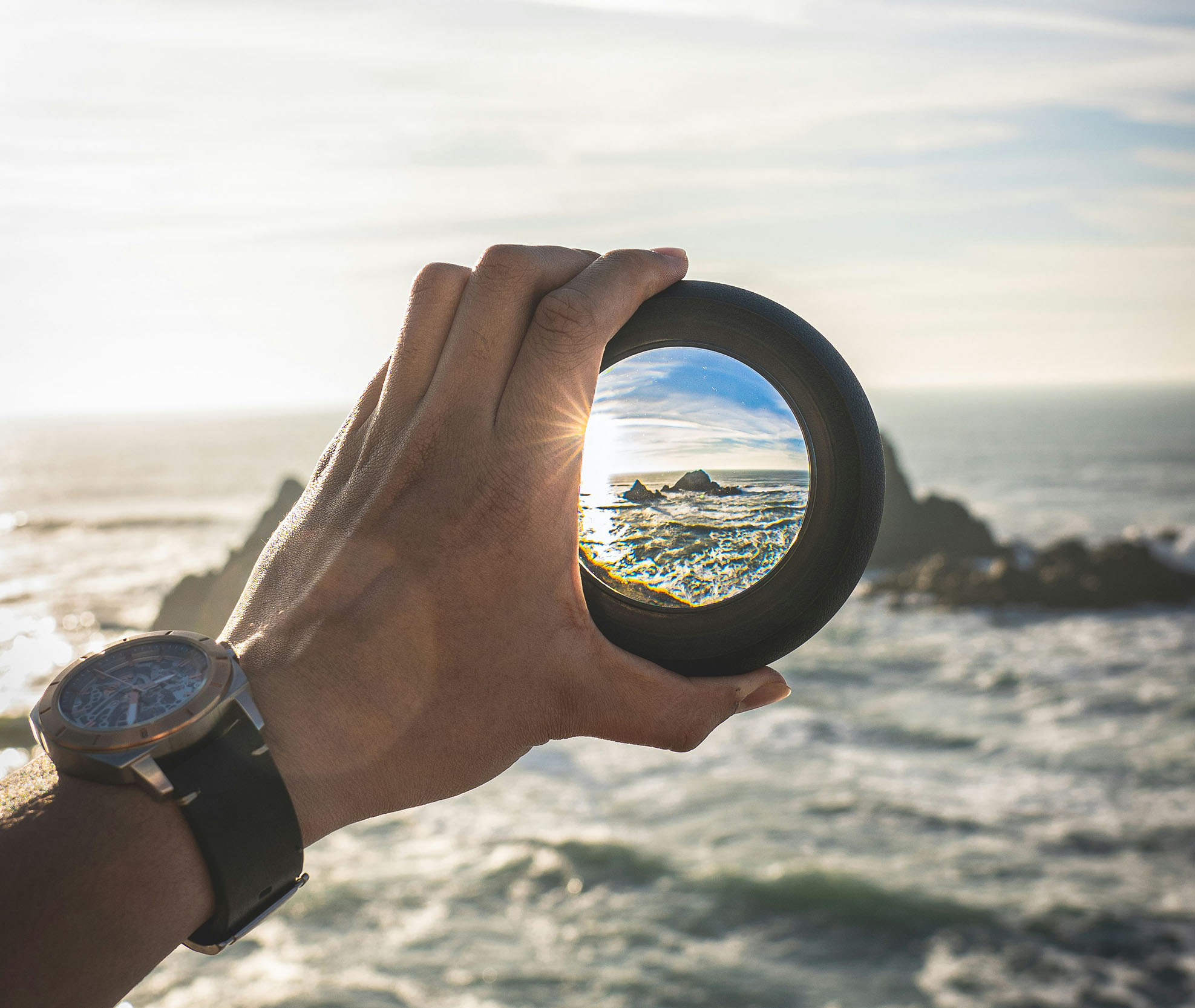 Sheaff Brock in the news, Dave Gilreath publications for ThinkAdvisor, hand holding a lens in front of the ocean and the sun shining through the lens