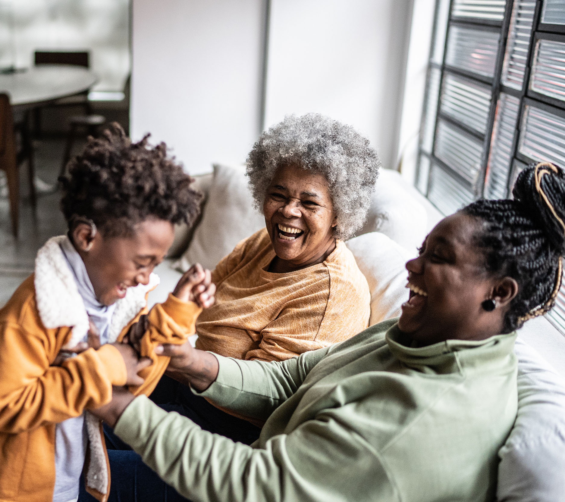 Sheaff Brock market update newsletters, August 2024, Black Millennial woman is sitting on the couch with her mom next to her and is playing with her young son